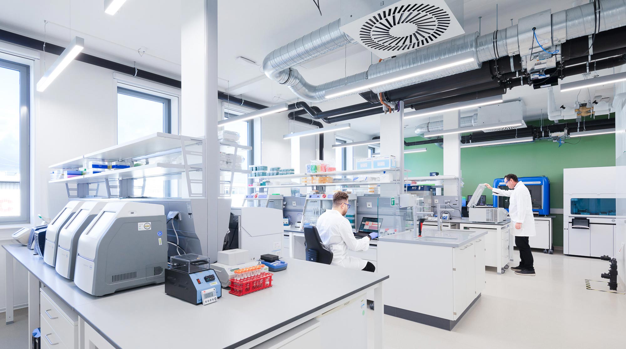 A couple of men in a room with white tables and computers.