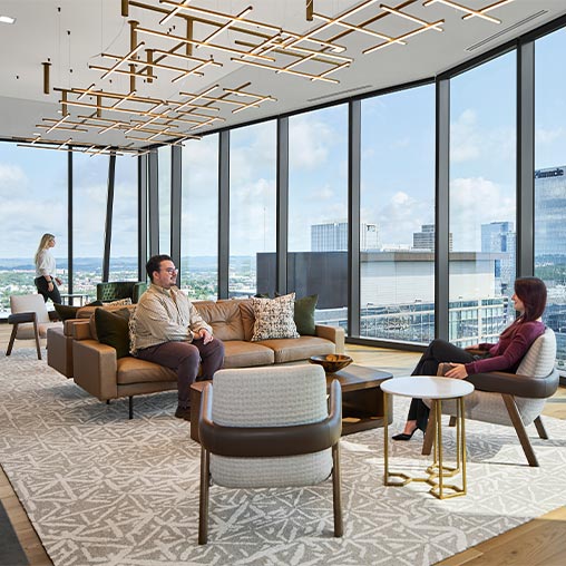 A man and woman sitting on a couch in a room with large windows.