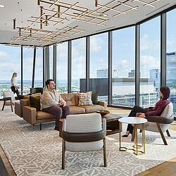 A man and woman sitting on a couch in a room with large windows.