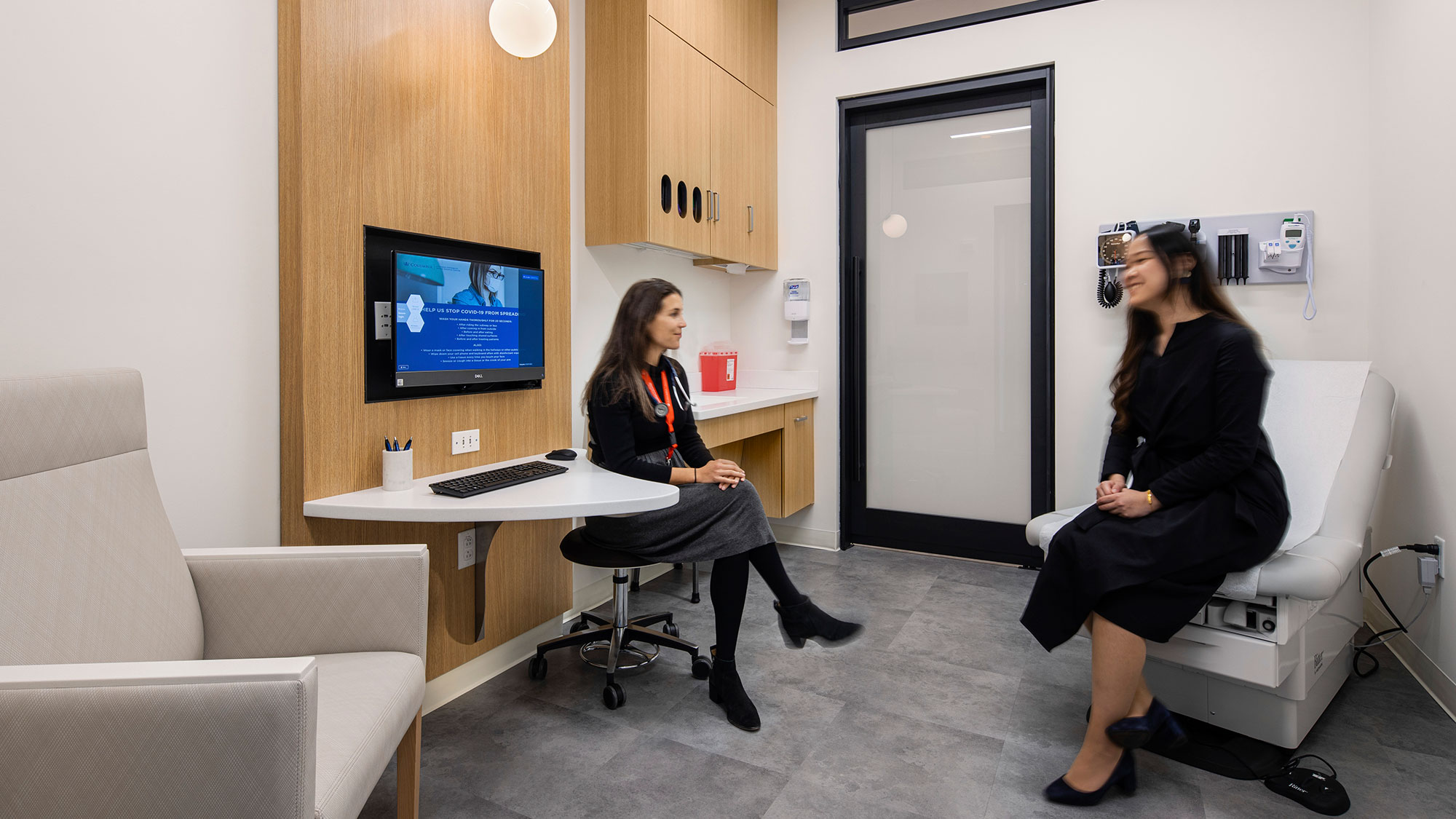 A couple of women sitting at a desk with a computer and a camera.