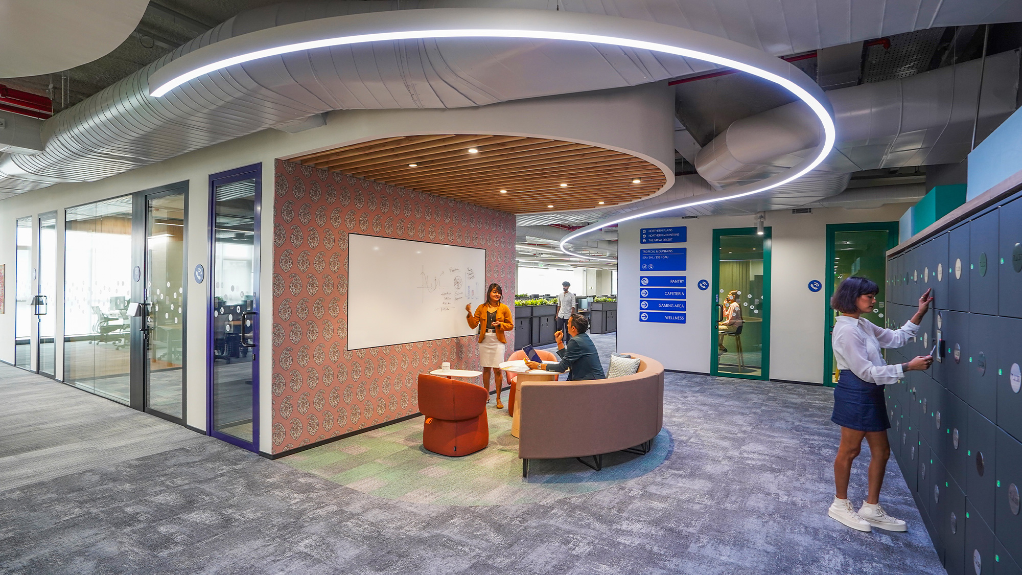 A person standing in a room with people sitting at tables and a large screen.