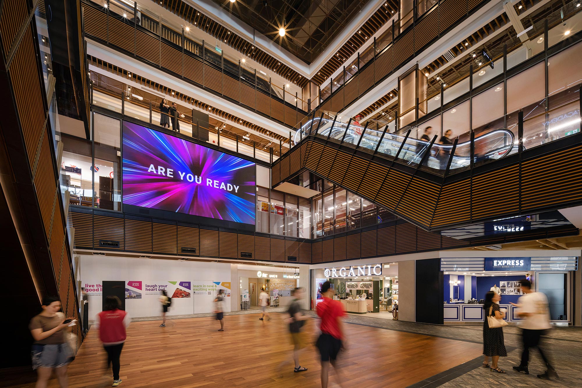 A group of people walking inside a building with a large screen.