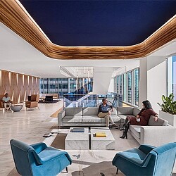 A man and woman sitting on a couch in a room with a large glass ceiling.