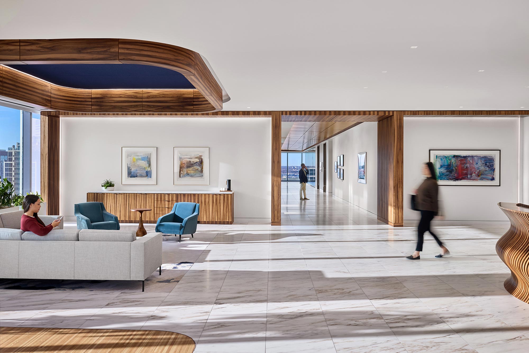 A woman sitting on a couch in a large room with a man standing.