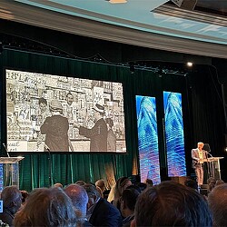 A person on a stage with a microphone in front of a crowd.