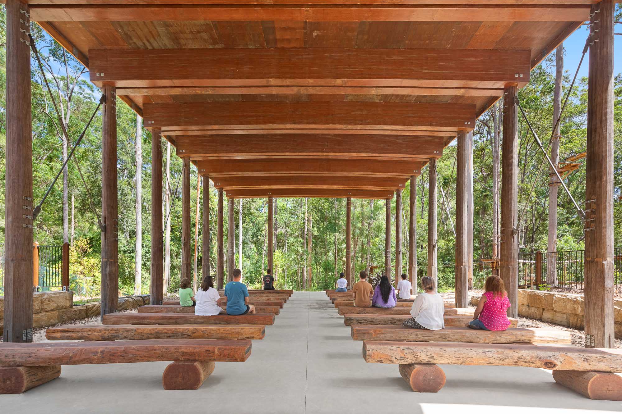 A group of people sitting on a wooden platform under a covered area.