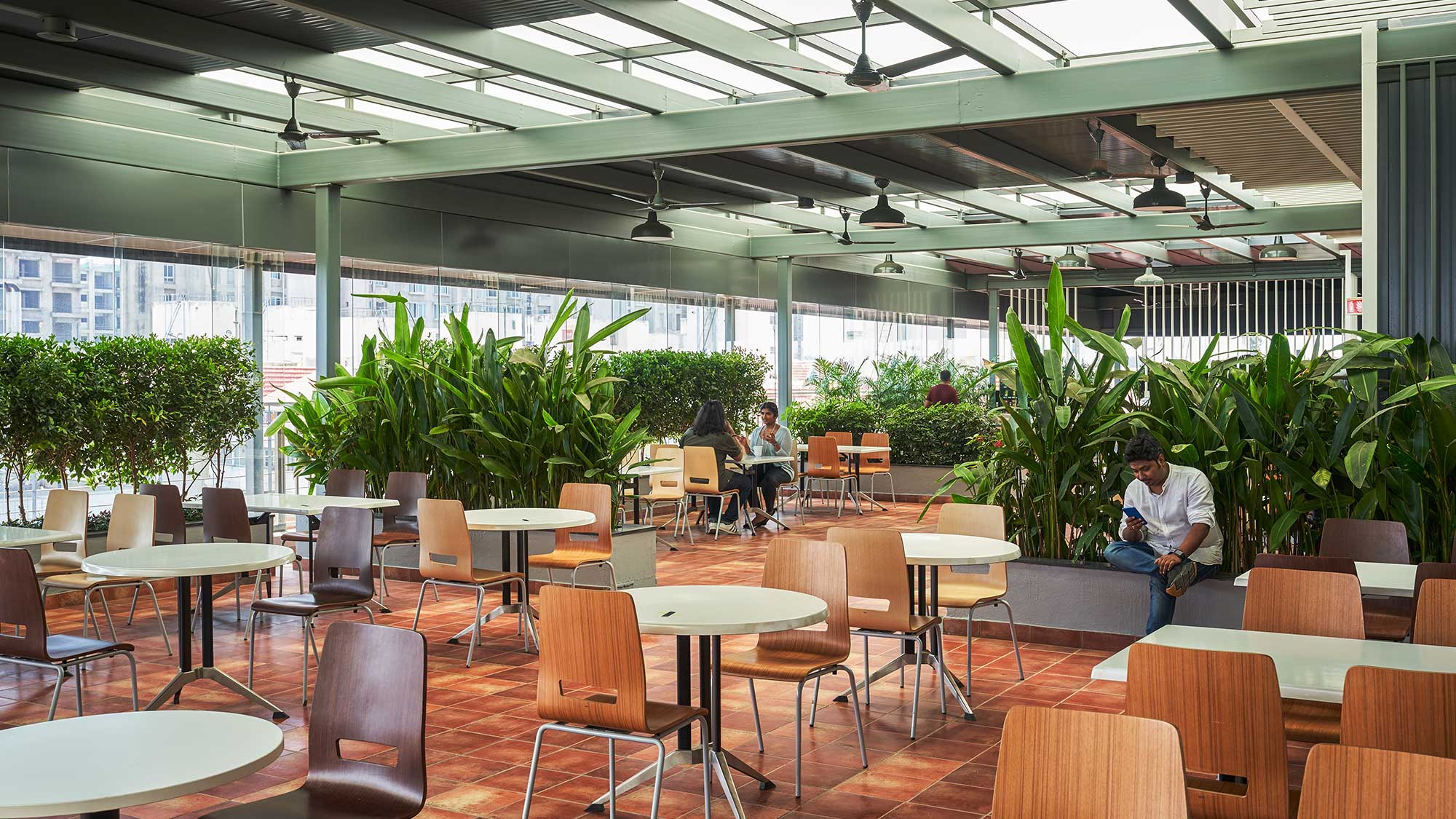 People sitting at tables in a large room with plants.