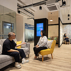 A man and a woman sitting in chairs in a room with a large screen.