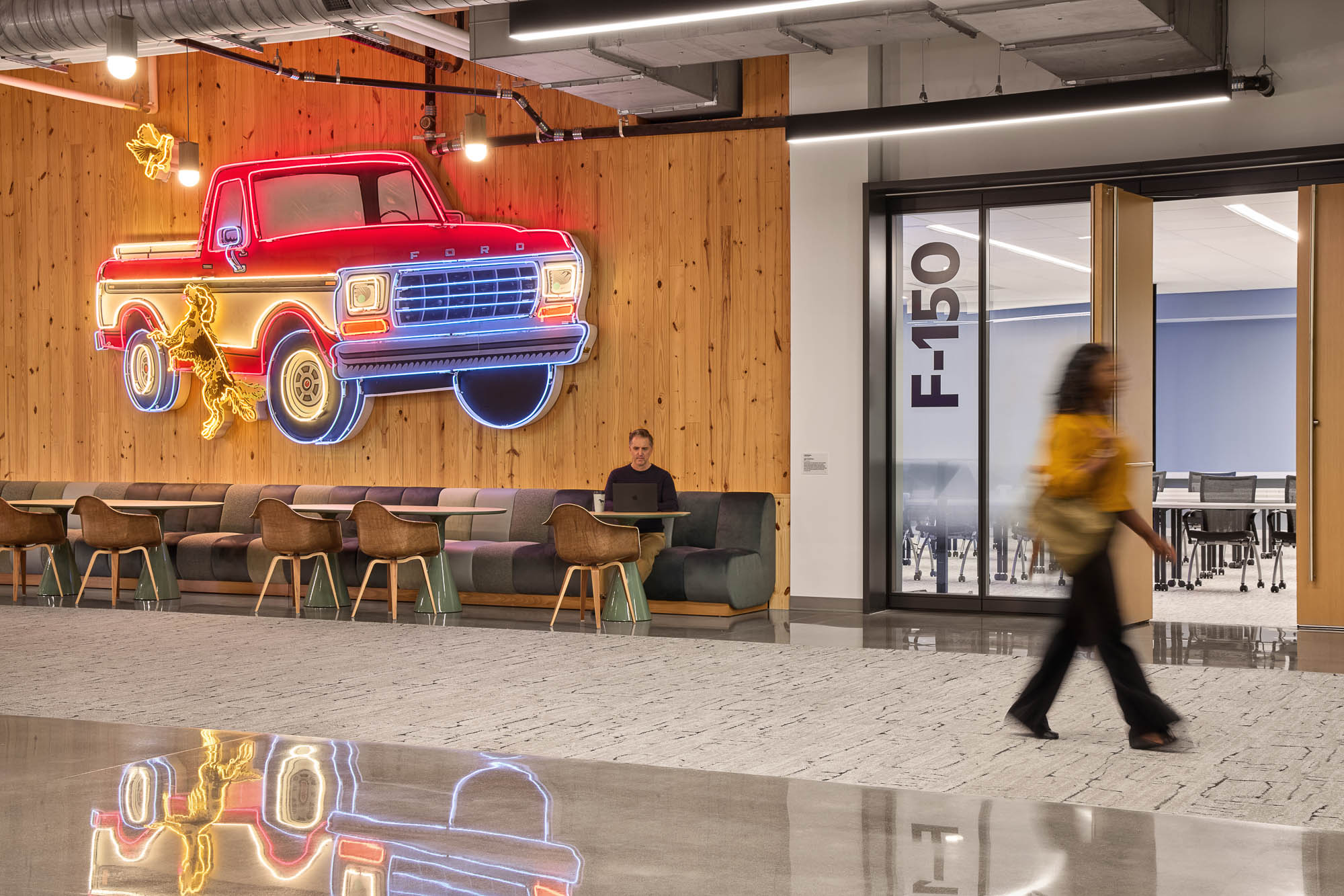 A person walking in a room with chairs and tables and a car.