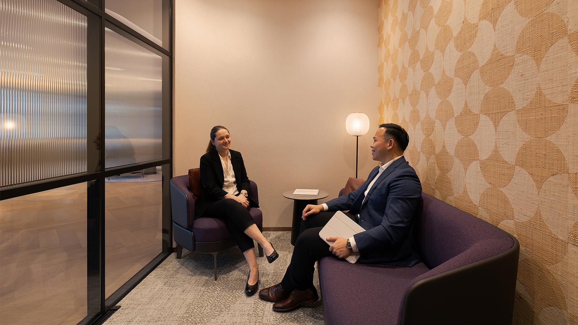 A man and a woman sitting in chairs in a room with a large window.