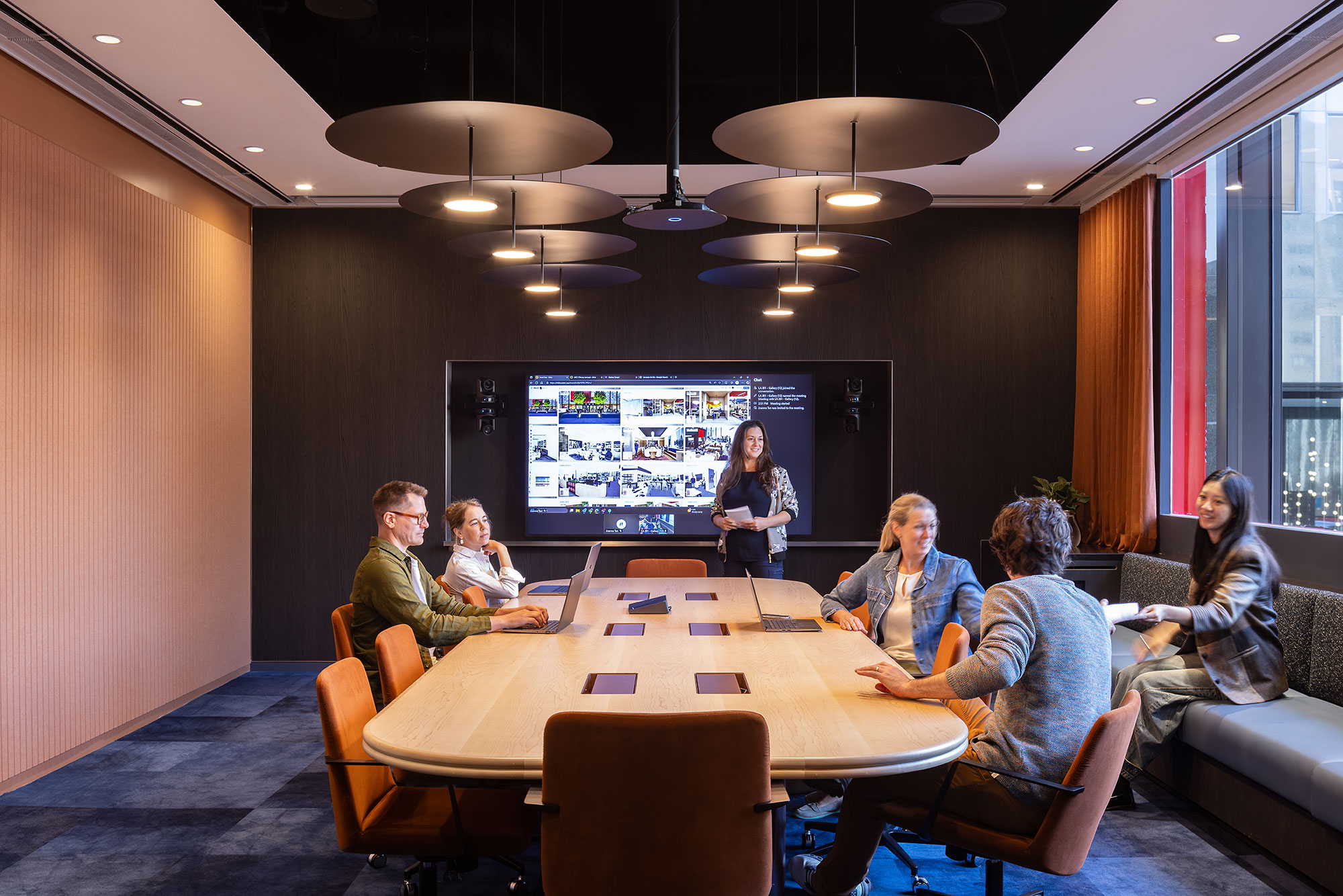 A group of people sitting around a table with a person standing in the middle of the room.