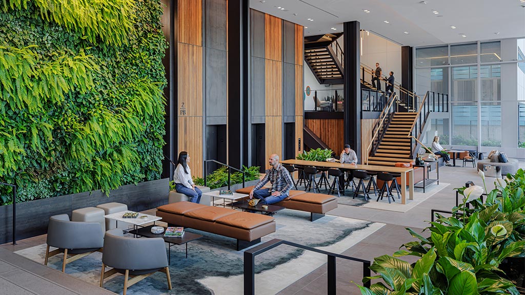 A group of people sitting in a room with a staircase and plants.