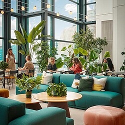 A group of people sitting in a room with plants and chairs.