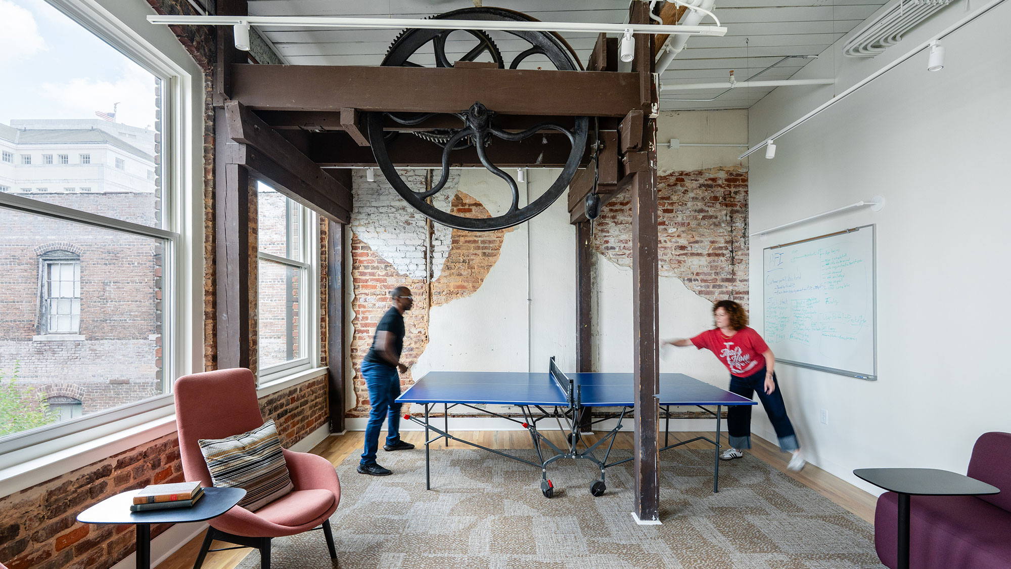 A couple of people playing ping pong in a room with a brick wall and a table and.