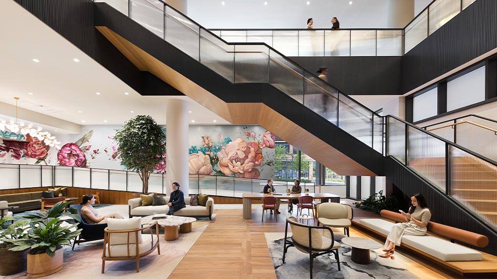 People sitting on couches in a room with glass walls and a staircase.