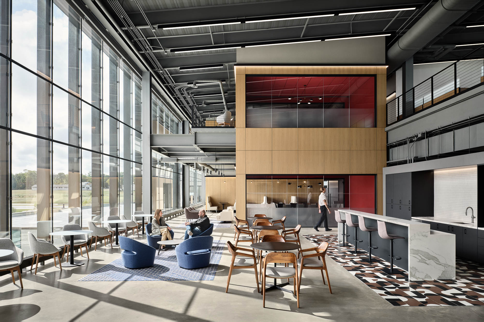 A group of people sitting at tables in a large room with windows.