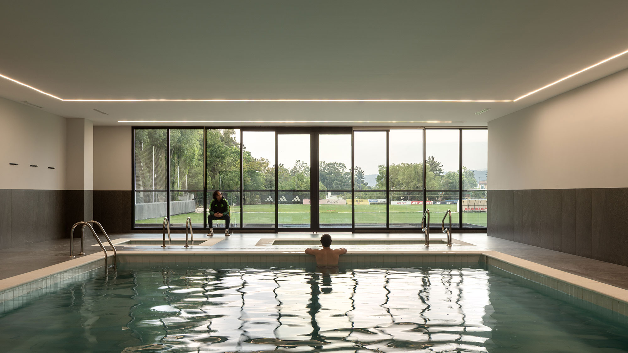 A man and a woman sitting in a large indoor swimming pool.
