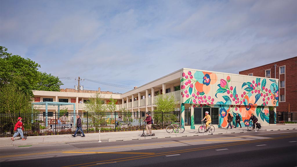 A group of people walking on a street next to a building with graffiti.