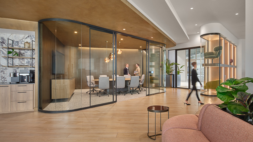A room with a glass door and a table with chairs and a couple people walking in it.
