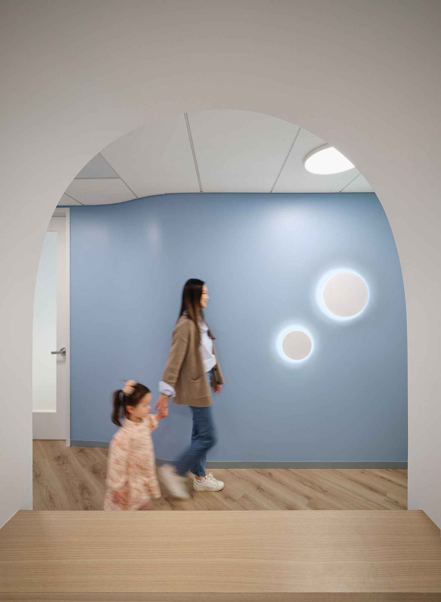 A person and a child walking in a room with a blue wall.