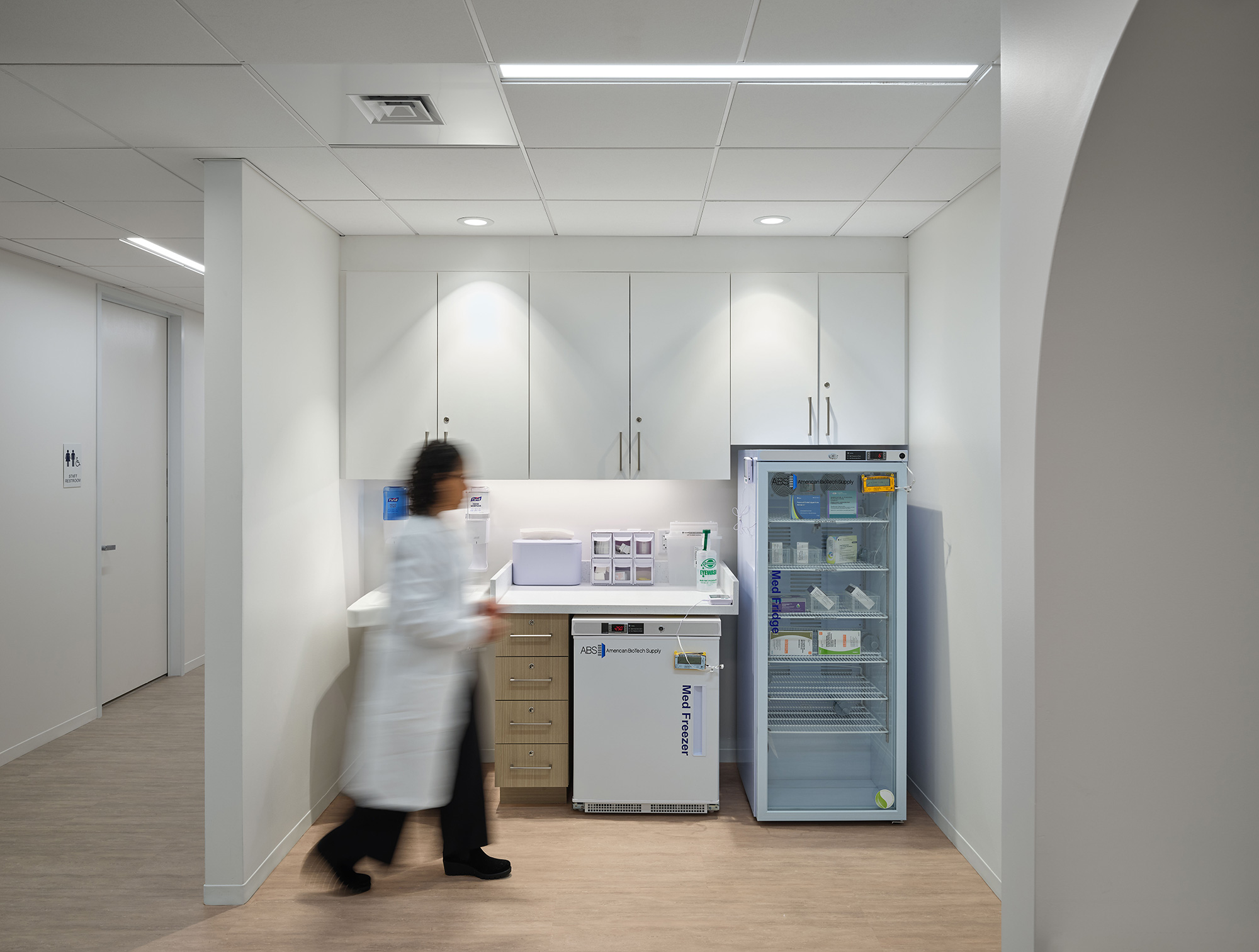 A person in a white coat in a room with white cabinets.