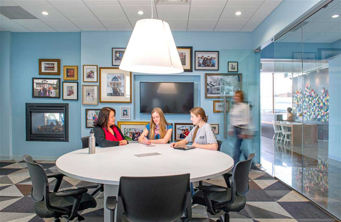 A group of women sitting at a table in a room with pictures on the wall.