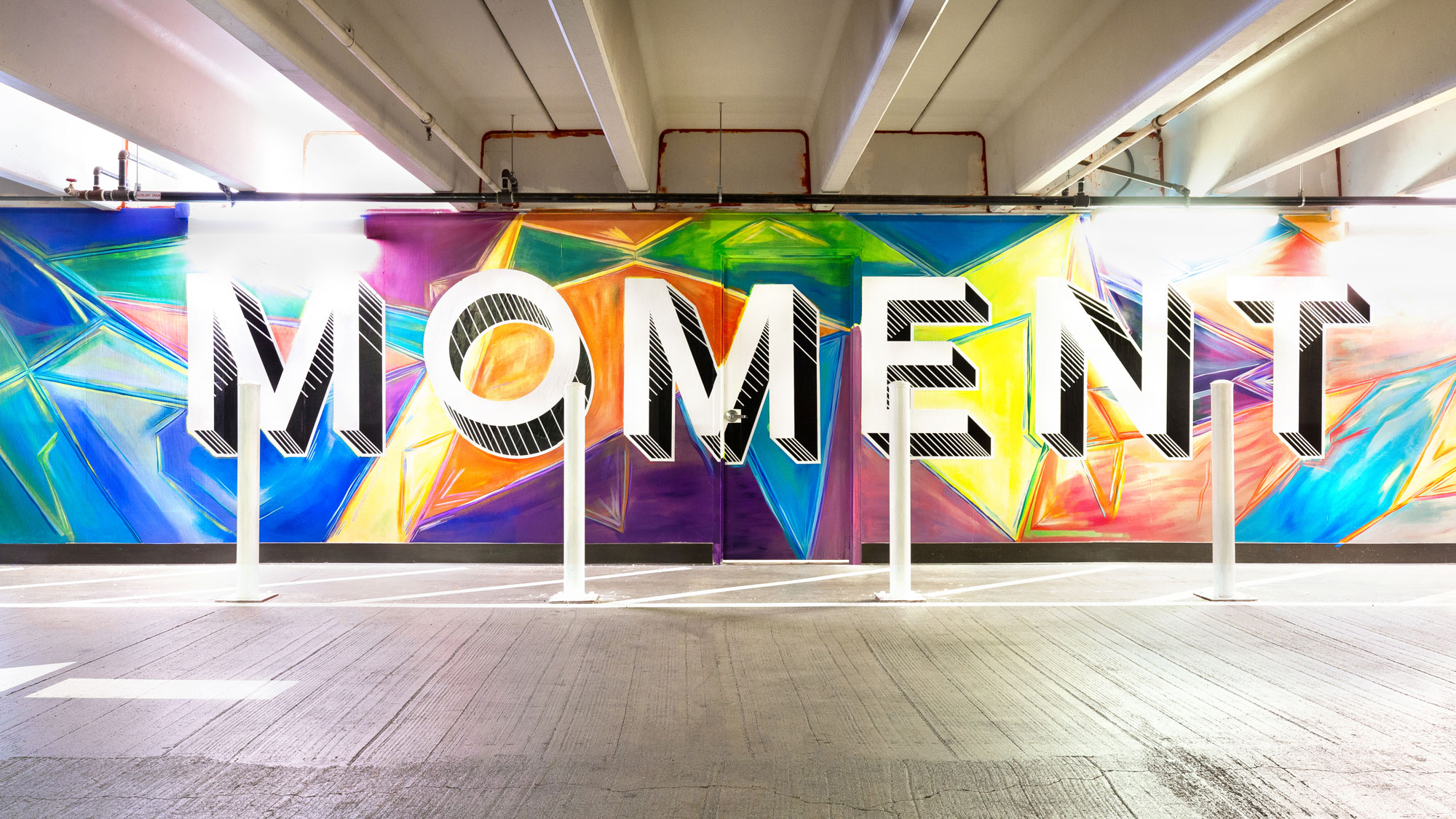 Colorful mural that reads "MOMENT" on a wall in a parking garage off of San Pedro Street in San Jose