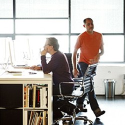 A person sitting on a chair next to a person sitting at a desk.
