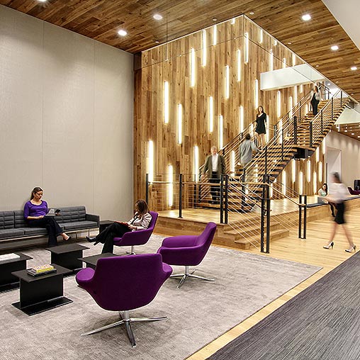 People sitting on benches in a large room with a staircase.