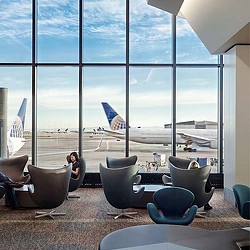 A person sitting in a chair in front of a window looking out at an airplane.