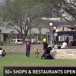 A person and a child walking on a lawn with balloons.