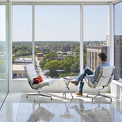 A person sitting in a chair looking out a window at a helicopter.