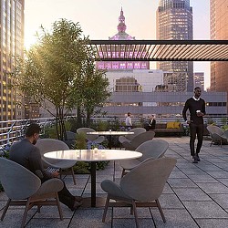 A group of people sitting at tables in a courtyard with tall buildings.