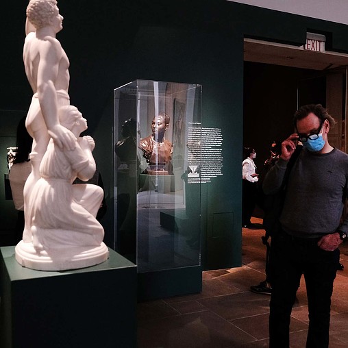 A person wearing a mask and a mask looking at a statue.