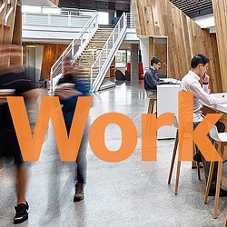 A group of people sitting at desks in a room with stairs.
