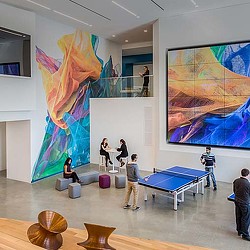 People playing ping pong in a room with large paintings.
