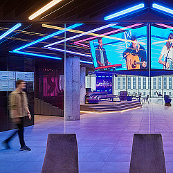A person walking in a large room with a large screen and a large poster on the wall.