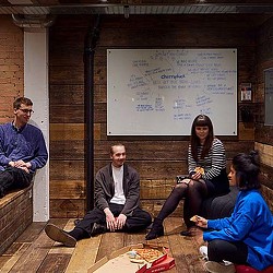 A group of people sitting on a bench in front of a whiteboard.