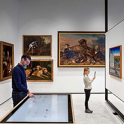 A man and a woman looking at art on the wall.
