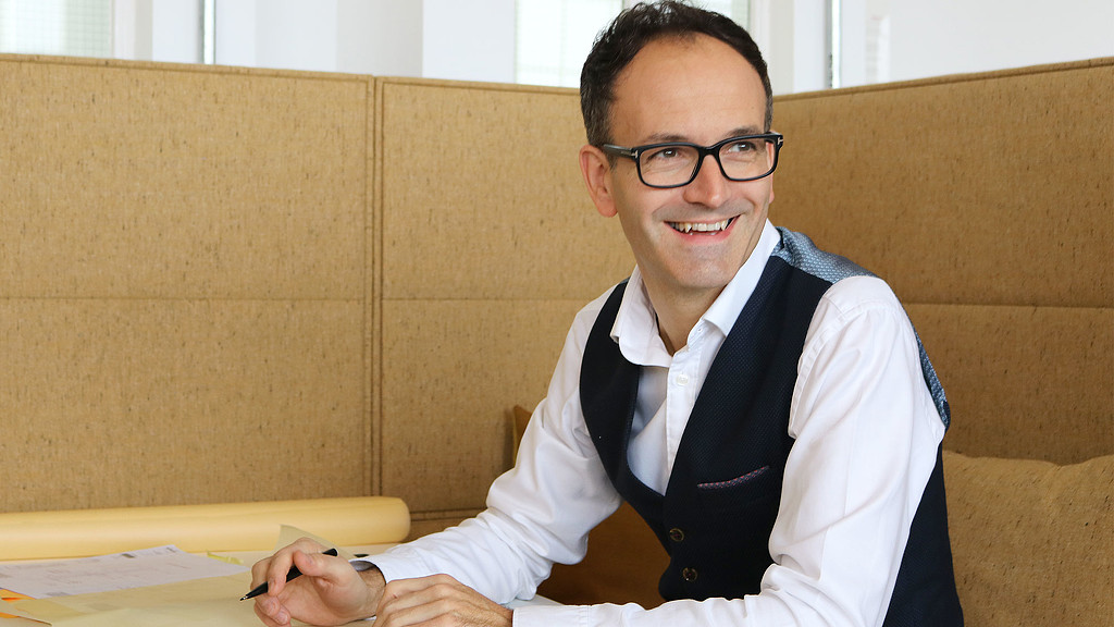 A man wearing glasses and a white coat sitting at a desk.