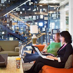 A man and woman sitting in a room with a staircase and a lamp.