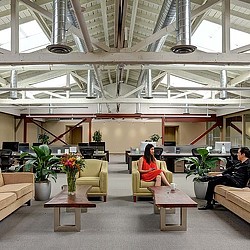 A couple of people sitting in a room with plants and a glass ceiling.