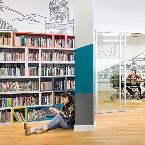 A person sitting on the floor in front of a bookcase.