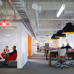 People sitting at desks in a room with a white wall and a large white board with black.