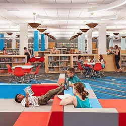 A group of people sitting on a red and white mat in a room with tables and chairs and.