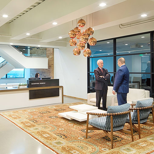 A couple of men standing in a room with a large glass table and chairs.