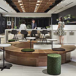 A person standing in a room with a green barrel and people sitting at tables.