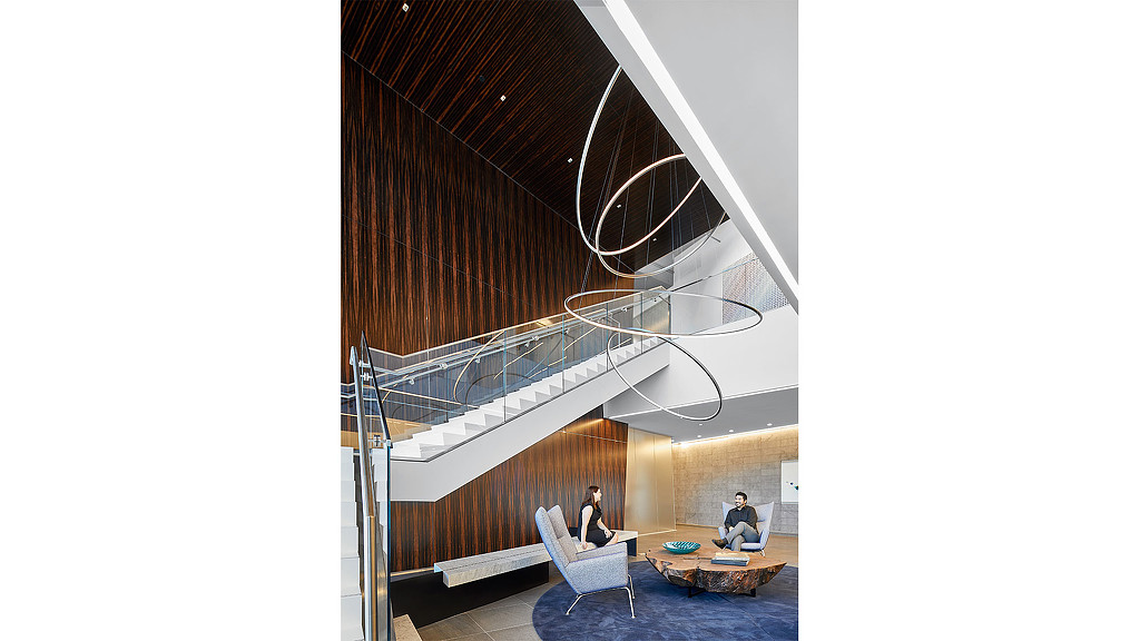 A couple of people sitting in a room with a staircase and a glass ceiling.