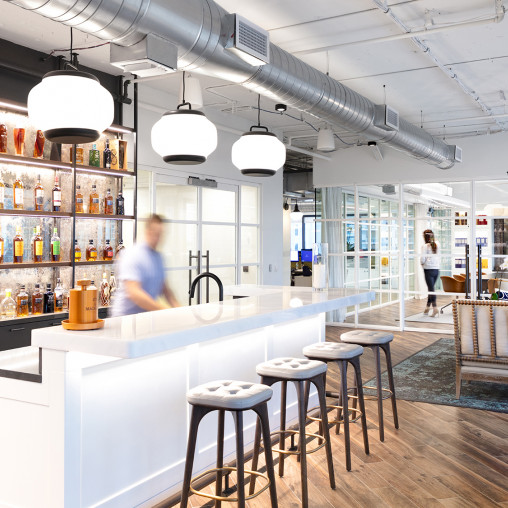A bar with stools and a couple people in the background.