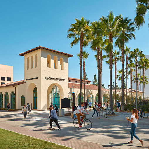 A group of people walking around a building with palm trees.